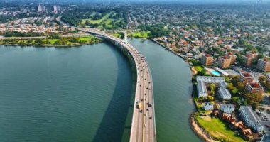 Arabalar güneşli bir günde köprüye ve karaya hareket eder. Nehrin karşısındaki köprüde yoğun trafik var. Üst görünüm.