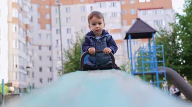 Tahterevallinin bir ucunda oturan tatlı çocuk. Oyun parkında kot ceketli bebek..