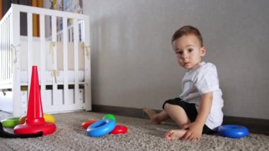 Beyaz erkek bebek yerde oyuncak piramitle oynuyordu. Çocuk kameraya döndü ve kaçtı..