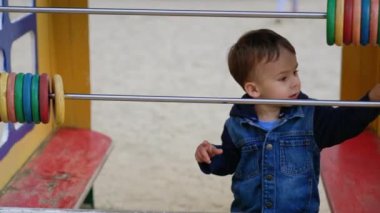 Oyun parkında kot ceket giyen küçük çocuk oynuyor. Tatlı çocuk büyük abaküste yüzüklerini hareket ettiriyor ve kaçıyor..