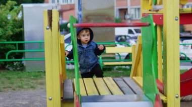 Kapüşonlu tatlı bebek merdivenle yavaşça yukarı çıkıyor. Dikkatli çocuk tırmanıp mutlu bir şekilde gülümsüyor..
