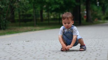 Güzel beyaz çocuk asfalt yolda çömelmiş oturuyor. Sevimli çocuk ellerindeki ve ayaklarındaki fayanslara ve sürüngenlere dokunuyor..