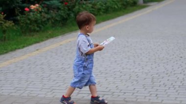 Kot pantolonlu şirin bir çocuk yolda yürüyor. Elinde dergi tutan bir çocuk, tahtadan oyulmuş büyük bir kedi heykelinin yanına gelir..