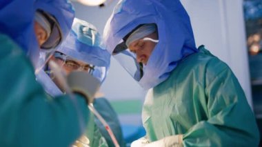 Operasyonda kask takan üç profesyonel sağlık görevlisi çalışıyor. Doktorlar artroskopik prosedür uyguluyorlar.