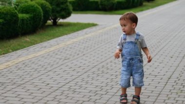 Asfalt yolda kot pantolon giymiş, çömelmiş şirin bir bebek. İlgilenen çocuk yerdeki fayanslara dokunuyor..