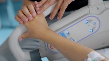 Kateterli kadın eli hastane tırabzanının yanında duruyor. Erkek elleri bir kadının elini okşuyor. Kapat..