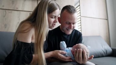 Kafkasyalı yeni doğmuş ebeveynler yeni doğan oğullarına sarılıyorlar. Ebeveynler kanepeye oturup bebek sallar ve onunla konuşurlar..