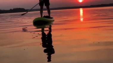 Erkek silueti nehire yansıyor. Gün batımında nehrin yukarısında duran bir erkek bacağının alt kısmı..