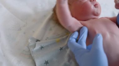 Sevimli çıplak yeni doğan bebek masada yatıyor. Sıhhiyenin eldivenli elleri, doğumda çocuğun parametrelerini ölçmek için mezura kullanıyor. Kapat..