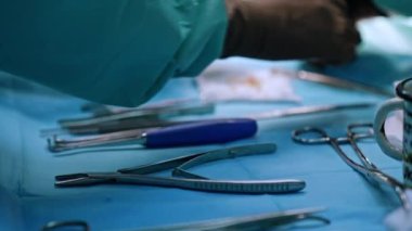Masadaki metal aletler ameliyat için hazırlandı. Lateks eldivenli sıhhiyecinin elleri aletleri alır. Kapat..