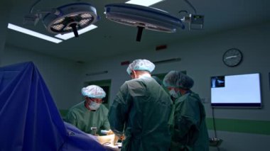 Bir grup erkek doktor ameliyathanede çalışıyor. Doktorlardan biri kısa çekiç ve keski kullanıyor. Yürüyerek ortopedik ameliyat.