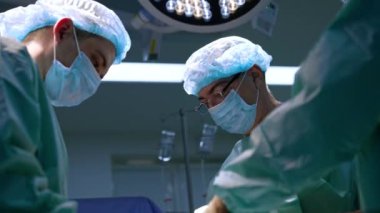 Üniforma giyen ve koruyucu maskeler takan profesyonel cerrahlar operasyonda çalışıyor. Düşük açı görünümü.