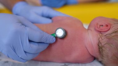 Doğum uzmanının eldiveni, yeni doğan bebeği incelemek için steteskop kullanıyor. Doktor bir çocuğun sırtına tıbbi cihaz takıyor. Kapat..