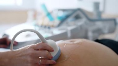 Doktor 'un eli, aleti büyük jöleli hamile karnına doğru hareket ettiriyor. Hamilelik gelişiminin ultrasonik incelemesi.