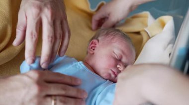 Sevgi dolu ebeveynler yeni doğan bebeklerinin yanında dururlar. Mavi tulumlu küçük bir çocuk babasının eliyle okşanıyor. Kapat..