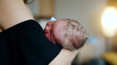 Annesinin kolunda uyuyan küçük bir bebeğin sarışın kafası. Tanınmayan anne bebeğini sallıyor. Kapatın. Bulanık arkaplan.