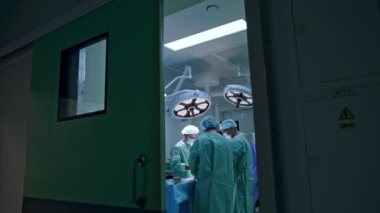 Modern, hafif operasyonel tiyatroda ameliyat yapan bir grup doktor. Ameliyathanenin kapısındaki görüntüler..