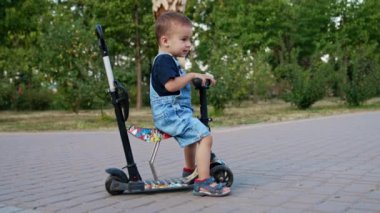 Scooter 'da oturan kot pantolonlu gülen çocuk. Mutlu bebek hareket etmek ve sürmek için topraktan itiyor.