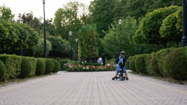 Bisikletin üzerinde oturan bir erkek bebeğin arka görüntüsü. Çocuk kafasını sallıyor ve kameraya doğru dönüyor. Yazın arka planda park et..