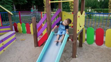 Parktaki kaydırağın yanında ayaklarını çarpan güzel bir bebek. Kot pantolonlu çocuk kaydırağın oraya gidiyor..