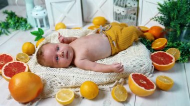 Sarı pantolonlu barışçıl yeni doğmuş bebek portakallarla çevrili. Stüdyoda mavi gözlü beyaz bir bebeğin görüntüsü..