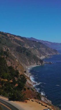 Okyanusla buluşan dağların muhteşem manzarası. Çam ağaçlarının arasındaki kayalıklardaki yollar. Kaliforniya 'daki Big Sur Morro Körfezi, ABD. Dikey video