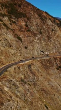 ABD 'nin Kaliforniya eyaletindeki Big Sur dağlarında bir otoyol. Mavi okyanus ve gökyüzünün arka planında muhteşem kayalar. Dikey video