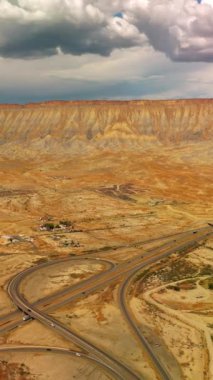 Güzel Kanyon dağları, çölleri ve ayaklarının dibinde küçük bir kasaba. Kasabanın sınırından ve çölden geçen yollara inen insansız hava aracı. Arkaplanda kayaların üzerinde dramatik bulutlar var. Dikey video