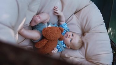 Sevimli beyaz bebek elinde bir ayıyla sallanan sandalyede yatıyor. Dışarıda dinlenen tatlı bir erkek bebek. Dikey ekran.