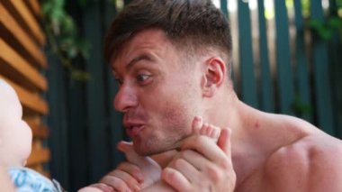 Beyaz bir baba tatlı bebeğiyle oynuyor. Mutlu baba bebeğe gülümsüyor ve çocuğun ayaklarını yüzüne koyuyor. Kapat..