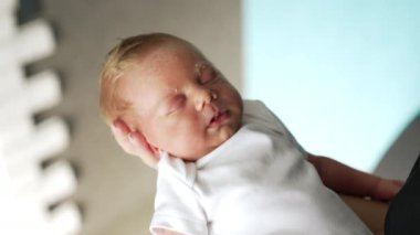 Beyaz elbiseli küçük bebek, ebeveynlerinin elinde huzur içinde uyuyor. Babasının parmağı küçük çocuğun burnuna değiyor. Kapat..