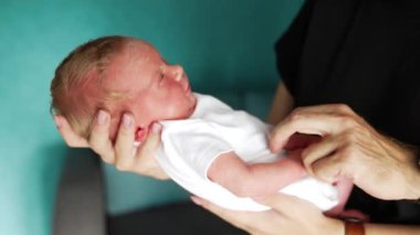 Beyaz elbiseli yeni doğmuş bebek yavaş yavaş uyanıyor. Babamın eli bebeğin karnını gıdıklıyor. Kapat..