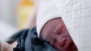 Doğumdan hemen sonra yeni doğmuş bir çocuğun mutsuz yüzü. Beyaz şapkalı bebek annemin göğsünde ağlıyor. Kapat..