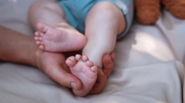 Babamın eli nazikçe küçük bir bebek ayağını tutuyor. Baba onlara dokunurken bebek ayaklarını savuruyor. Kapat..