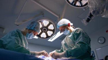 Doktor ve hemşire çok çalışıyor. Cerrah kesiği dikiyor ve hemşire ipliği kesiyor. Düşük açı görünümü.