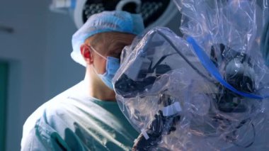 Odaklanmış erkek doktor dikkatlice mikroskoba bakıyor. Modern yenilikçi ekipman kullanımı ile cerrahi.