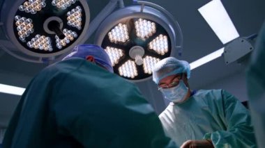 Deneyimli erkek cerrahlar birlikte çalışırlar. Doktorların tavanında iki büyük yuvarlak lamba var. Düşük açı görünümü.