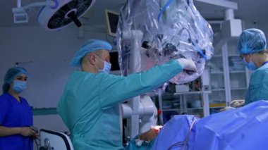 Cerrahlar enstrümanı hemşireye verirler. Doktor plastikle kaplı mikroskopu yakına çeker ve hastanın gözlerine ve vücudundaki kesiğe göre ayarlar..