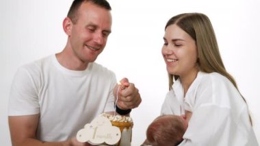 Mutlu bir aile, çocuk hayatının ilk ayını pastayla kutluyor. Yenidoğan 'ı annesi emziriyor. Beyaz arkaplan.