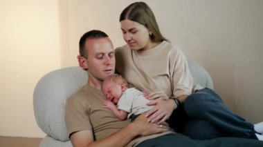 Mutluluk portresi. Kanepede oturan beyaz bir çift ve babasının göğsünde uyuyan küçük bir çocuk..