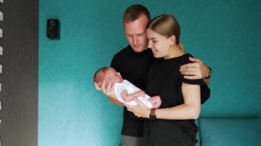 Yeni doğmuş çocukları olan beyaz bir çifti seviyorlar. Anne bebeğine şefkatle bakıyor ve baba çocuğun kafasını okşuyor..