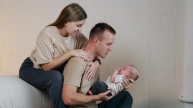 Üç kişilik sevimli beyaz bir aile. Erkek, kanepeye bebek oturtur ve kadın da kocasına sarılır..