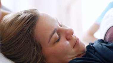 Daha yeni bir bebek doğurmuş bir kadının yüzü. Yeni doğmuş bir anne yeni doğmuş bir bebeği göğsünde tutuyor ve kocasına gülümsüyor. Kapat..