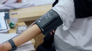 Hamile bir kadına kan basıncını ölçüyorum. Tanınmayan bir bayan kolunda kemerle oturuyor ve kocasının eli karnını okşuyor..