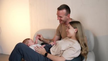 Sevgi dolu ebeveynler yeni doğmuş bebekleriyle vakit geçiriyorlar. Baba, çocuğu küçük ellerinden tut ve anne de ayaklarını tut..