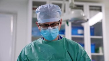 Erkek cerrah gözlüklerden aşağı bakıyor. Modern ameliyathanede çalışmaya odaklanmış bir doktorun portresi..