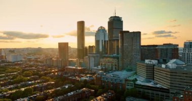 Boston, Massachusetts, ABD 'de güneş batıyor. Düşük katlı apartmanların üstündeki İHA görüntüleri gökdelenlerden uzaklaşıyor..
