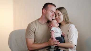 Üç kişilik mutlu bir aile. Kafkasyalı ebeveynler yeni doğan bebeklerini kucağına alıp ona yaslanıyorlar..