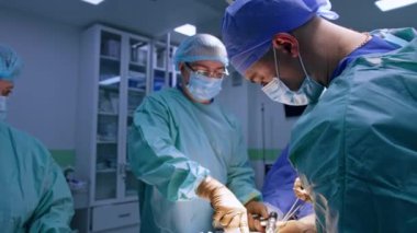 Cerrahi cihazı tutan baş cerrah ve ameliyat edilen bir hastanın ayağı. Doktora yardım etmek için metal forseps kullanılıyor. Kadın hemşire enstrümanlarla masada duruyor..