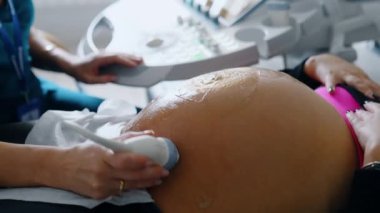 Üzerinde jöle olan hamile bir kadının koca göbeği. Doktorun eli ultrason cihazını hastanın karnına taşıyor. Kapat..